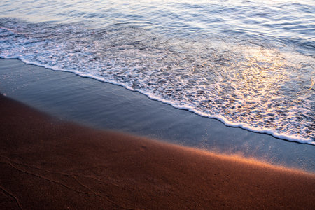 Black magnetite sand and sea waves under sunset rays, copper highlights on sand, blurred seascape background. High quality photoの写真素材