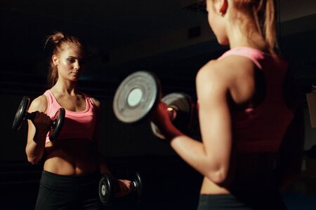 Young girl doing exercise for biceps with dumbbellsの写真素材