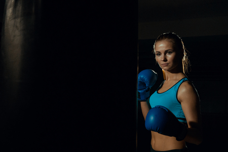 Girl boxer in blue boxing gloves near a punching bag.の写真素材
