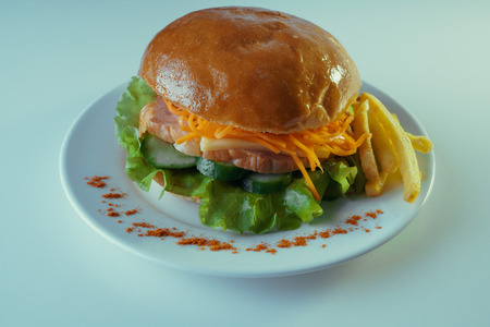 A large and tasty hamburger with a juicy piece of chicken, cucumbers, Korean carrots and cheese. On a plate with french fries.の写真素材