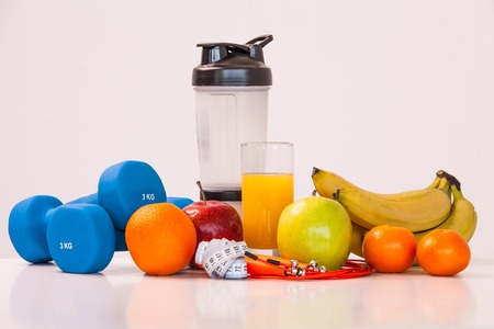 The concept of a healthy diet. Fintes meals. Sport lifestyle. Dumbbells. Shaker. Oranges. Apples. Bananas. fruit juice. The skipping rope. Measuring tape waist. on a white background. studio shooting.の写真素材