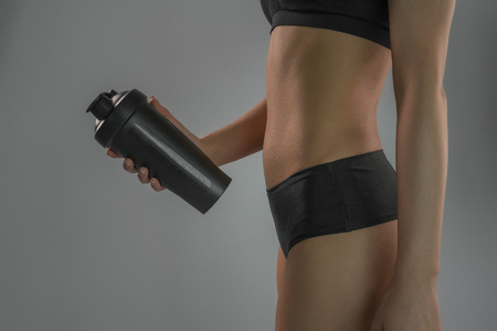 A girl with a sports figure holds a shaker on a gray backgroundの写真素材