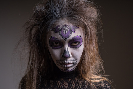 Portrait of a girl with a painted mask of a dead person on her face, isolated on a dark background....