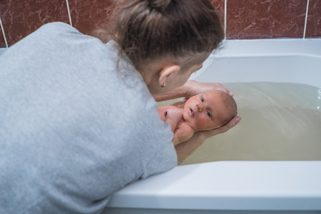 Woman bathing baby in the bath. Baby massage in warm water. Recoveryの写真素材