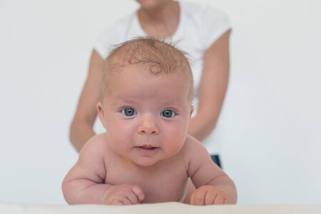 A funny baby is looking straight into the camera and a woman is holding a baby in the background.の写真素材