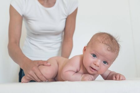 Portrait of smiling baby with big eyes lying on changing table and woman holding him from behind