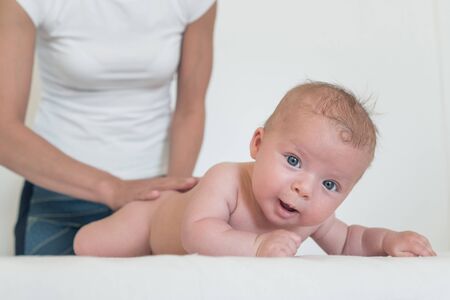 Portrait of smiling baby with big eyes lying on changing table and woman holding him from behindの写真素材