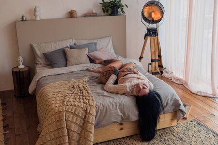 Sexy tattoo girl in panties and warm sweater posing lying on the bed head downの写真素材