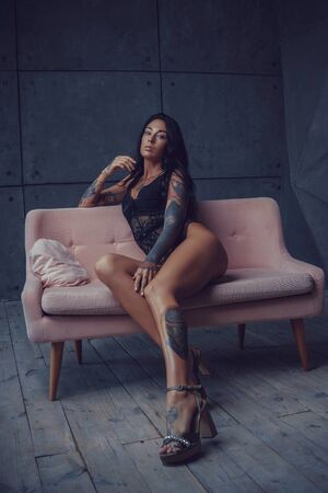 Beautiful brunette sitting on heels and in erotic lingerie posing sitting on the couchの写真素材
