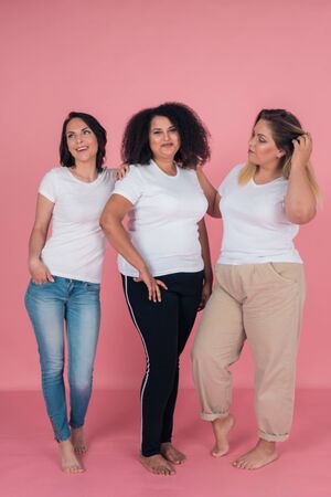Three girlfriends smile beautifully and pose for the camera on a pink background. Girls in white t-shirts. Layouts for designの写真素材