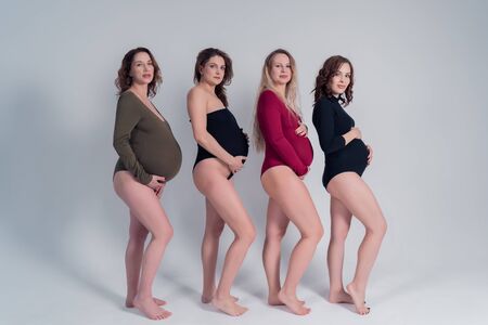 Four beautiful pregnant girls in bikinis stand each other on a white background.の写真素材