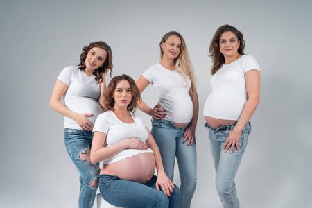 Four pregnant women in jeans and white shirts in the Studio on a black background.の写真素材