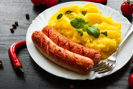 fried meat sausages with mashed potatoes in a plate on dark wooden backgroundの写真素材