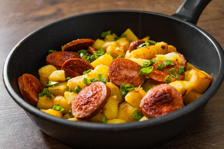 Roasted Potato and Sausage in frying pan on wooden tableの写真素材