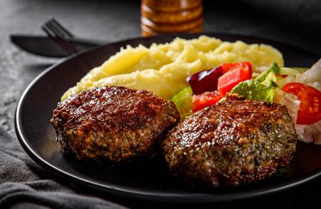 burger with mashed potatoes and vegetables salad on a black plate on Dark grey black slate backgroundの写真素材