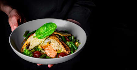 chef in a black suit holds in his hands bowl with salad on Dark grey black background