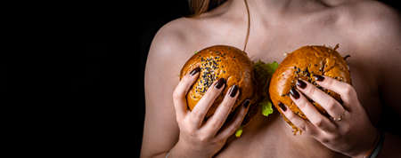Young naked woman keep in her hands tasty burgers on black backgroundの写真素材
