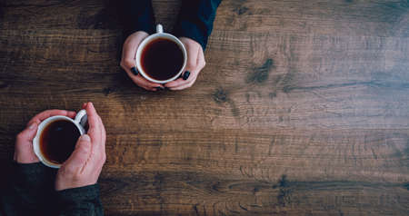Cups of black tea or coffee in the hands of men and women. on a wooden background. with copy space. top viewの写真素材