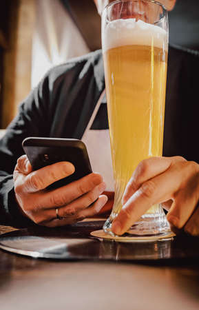 close up of man hand hold smartphone, drinking beer and reading message at bar or pubの写真素材