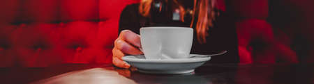 woman hands holding a white cup of tea or coffee standing on the table in cafeの写真素材