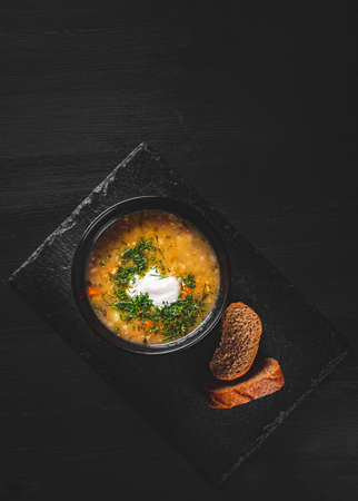 Soup with pickled cucumbers and pearl barley in black bowl on black wooden table backgroundの写真素材