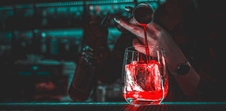 Closeup shot of bartender hand making negroni cocktail. Negroni classic cocktail and gin short drink with sweet vermouth, red bitter liqueur and dried orange garnish.の写真素材
