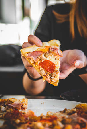 woman Hand takes a slice of meat Pizza with Mozzarella cheese, salami, Tomatoes, pepper, ham, Spices and chicken in cafeの写真素材