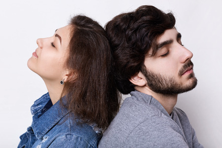 A young hipster couple sitting at home head to head relaxing with their eyes closed. Bearded man and...