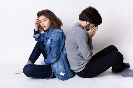 Feelings and attitudes. A couple sitting on the floor backs having tired and sad expression after a...