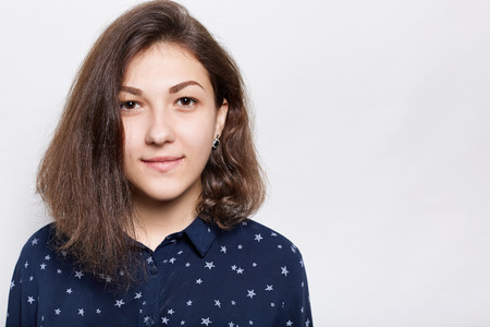 Half profile of young attractive female with dark charming eyes and with fashionable haircut, dressed in stylish shirt wearing black elegant earrings looking directly into camera.の写真素材