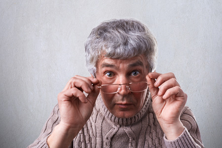 A close-up of surprised adult with gray hair and wrinkles wearing glasses. A senior man touching his...