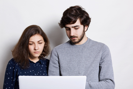 Stylish bearded man and beautiful woman standing close to each other enjoying modern technologies, using high-speed internet connection and laptop, browsing social media . の写真素材