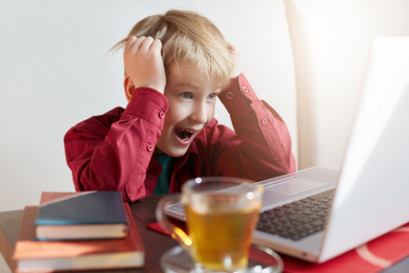 Childhood, modern technology, internet and education concept.Emotional adorable blond male having...