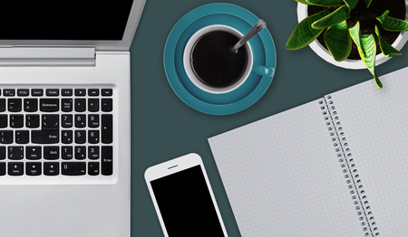 Office desktop with various objects. Laptop, cup of coffee or tea, smartphone and blank notebook laying on office desk. Workspace of business person. Top view office desk mock up with gadgetsの写真素材