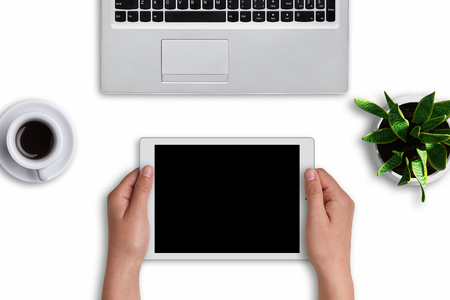 Woman`s hands holding modern tablet with blank screen over white background. Modern devices: tablet and laptop computer on white surface with cup of coffee and flowerpot with flower. Office designの写真素材