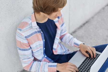 Cropped shot of stylish male student working at his course paper typing at laptop computer necessary information. Young boy using computer for surfing social networks using free internet conncetionの写真素材