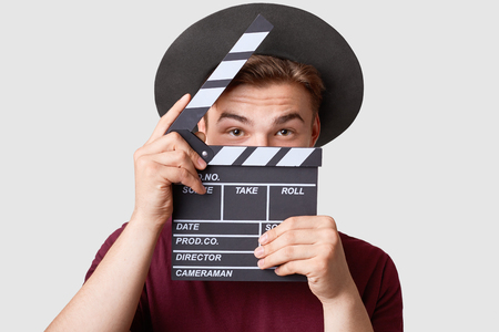 Professional male actor ready for shooting film, holds movie clapper, prepares for new scene, wears special clothes, isolated on white background. Handsome young man poses with clapboard in studioの写真素材