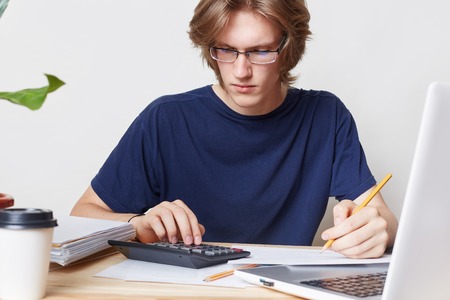 Attractive man faces financial crisis, studies notification from bank, calculates figures. Male student studies math, prepares report, calculates figures. People, business, occupation conceptの写真素材