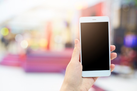 Woman`s hands holds modern electronic gadget. Unrecognizable female with white mobile phone and blank black screen for your advertisment or promotional text. Communication and technology conceptの写真素材