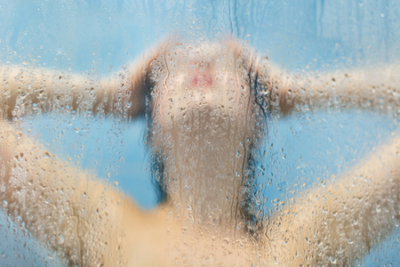 People and care concept. Silhoette of beautiful nude woman poses in shower cabine, takes douche, takes care of her skin, poses aginst dewy sweat glass with drops. Washing and wellness conceptの写真素材