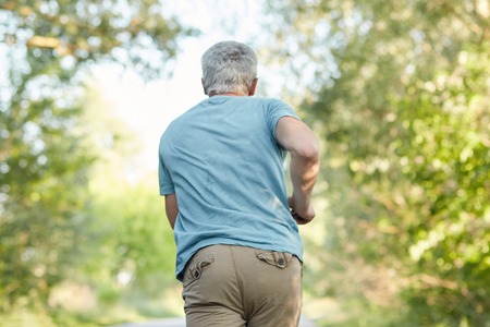 Back view of mature male joggs outside, has morning workout, enjoys sunny day and fresh air, being in motion, has healthy lifestyle. Elderly people, sport, motivation and retirement concept.の写真素材