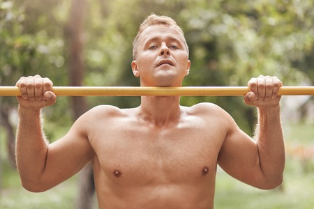 Hardy robust athletic man with bare body, does pull ups, works on his body, looks directly at camera...