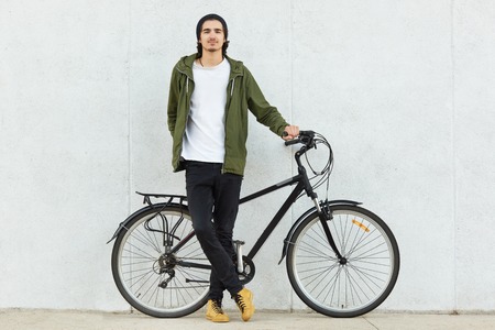Isolated shot of stylish hipster male teenager dressed in stylish outfit and sneakers, stands near...
