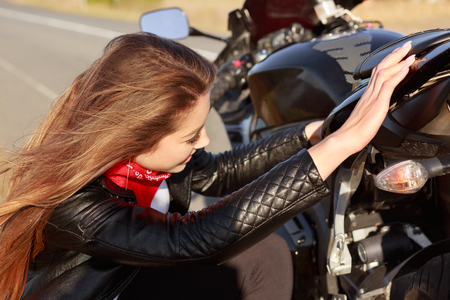 Female motorist tries to solve problem with transport, repairs motorbike during trip, fixes some parts, stops on road, being talented biker.の写真素材