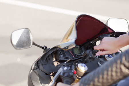 Unrecognizable female biker turns on engine of motorbike, keeps hand on key, ready to ride, poses against asphalt background, likes adventures and active lifestyle. Transport and extreme conceptの写真素材