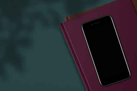Top view of modern mobile phone with blank empty display on book or notepad, against green...