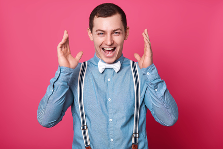 Close up studio portrait of glad handsome confident stylish man. Lucky guy raises hands up happily.の写真素材