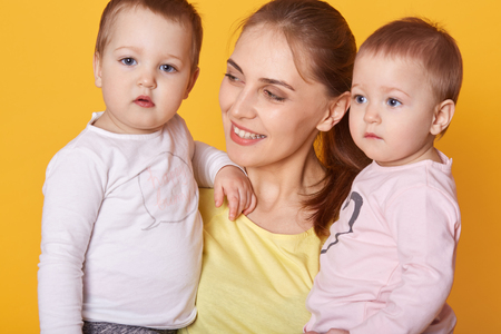 Portrait of young mother holding her little twins, cute active infants being interested to be...