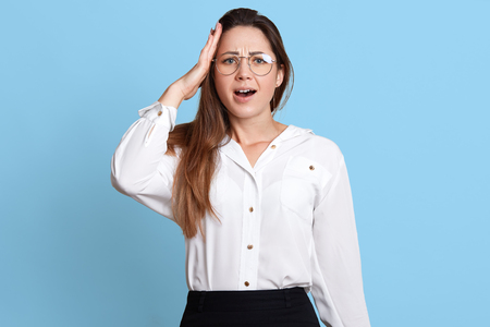 Worrying busy accountant holds her hand on head, remembers about important work assignment, opens her mouth with surprise. Slender attractive woman is short of time to complete all working tasks.の写真素材