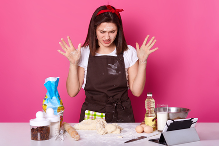 Close up portrait of tired housewife or baker looks sad, spends lots hours preparing Easter cake has, can not make dough desired consistency, wants to stop baking, isolated on pink background.の写真素材